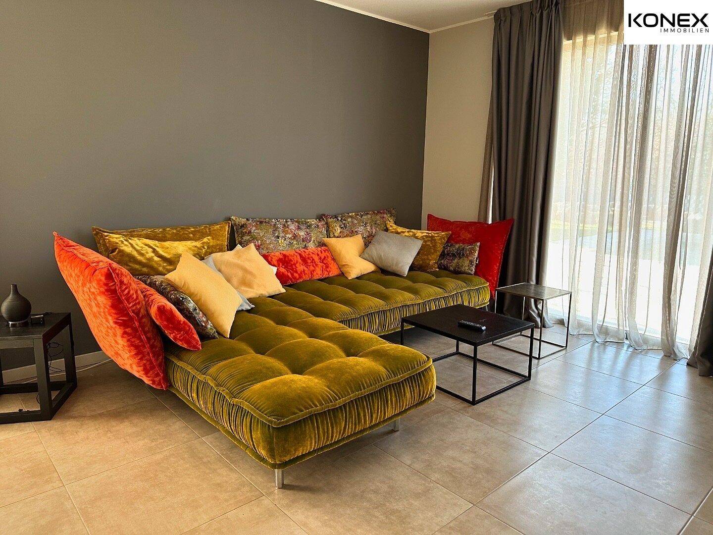 Gemütliches Wohnzimmer mit großem, farbenfrohem Sofa, Fliesenboden und viel Tageslicht.
