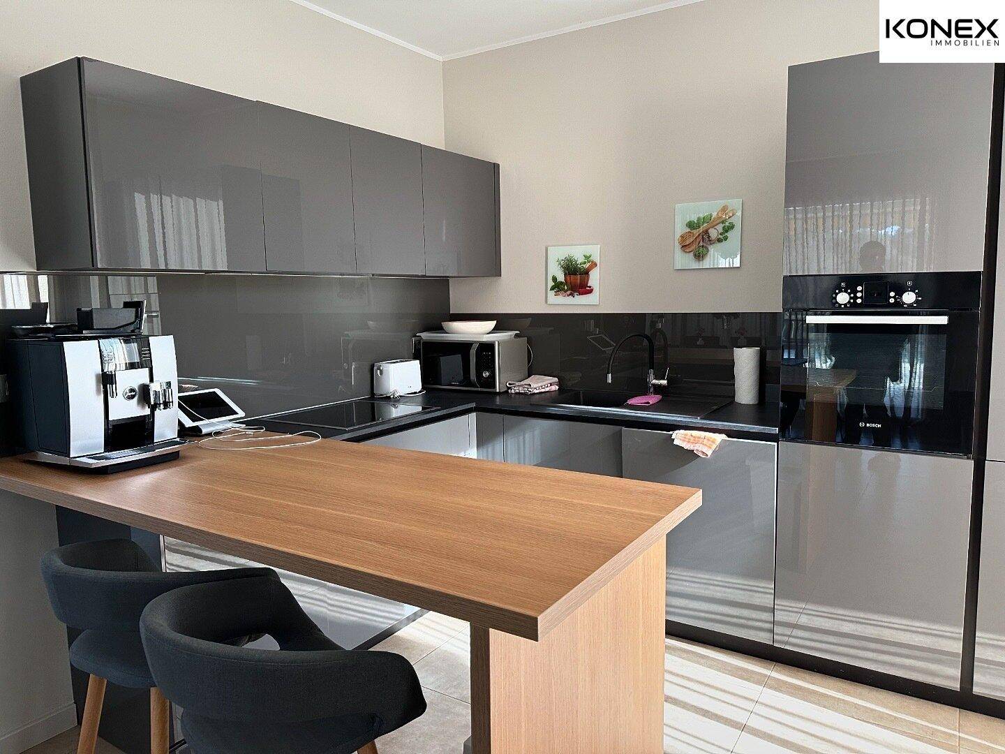 Moderne Küche mit grauen Hochglanzfronten, integrierten Geräten und praktischer Frühstücksbar.