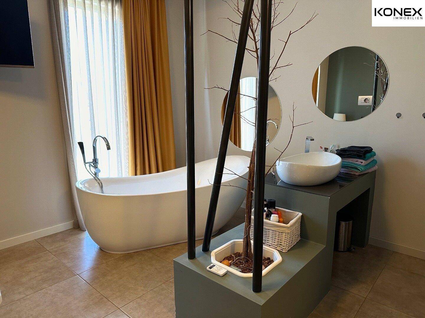 Geräumiges Badezimmer mit freistehender Badewanne, modernem Waschbecken und Fliesenboden.