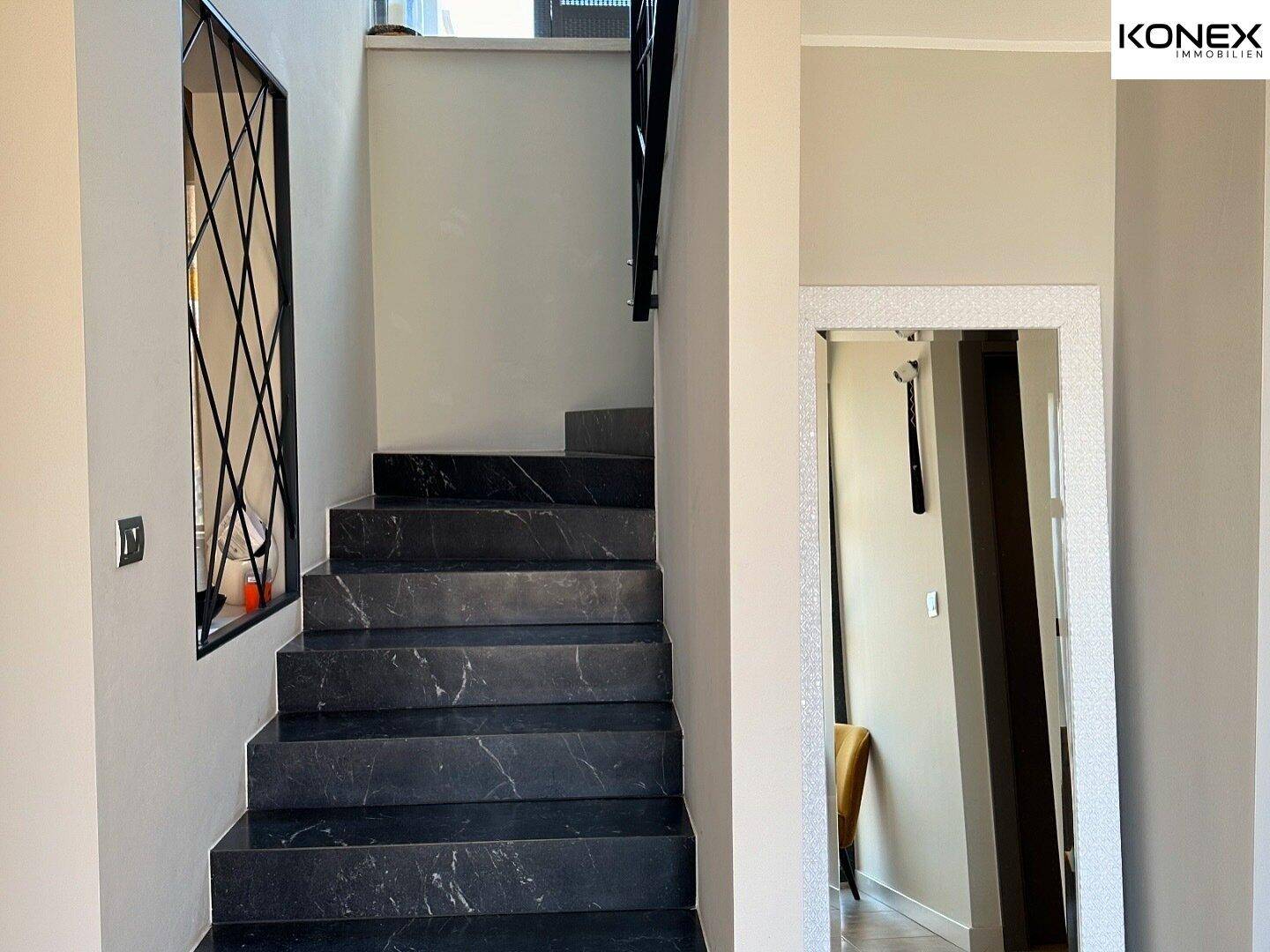 Elegante Treppe mit dunklen Marmorstufen und modernem Metallgeländer im Eingangsbereich.