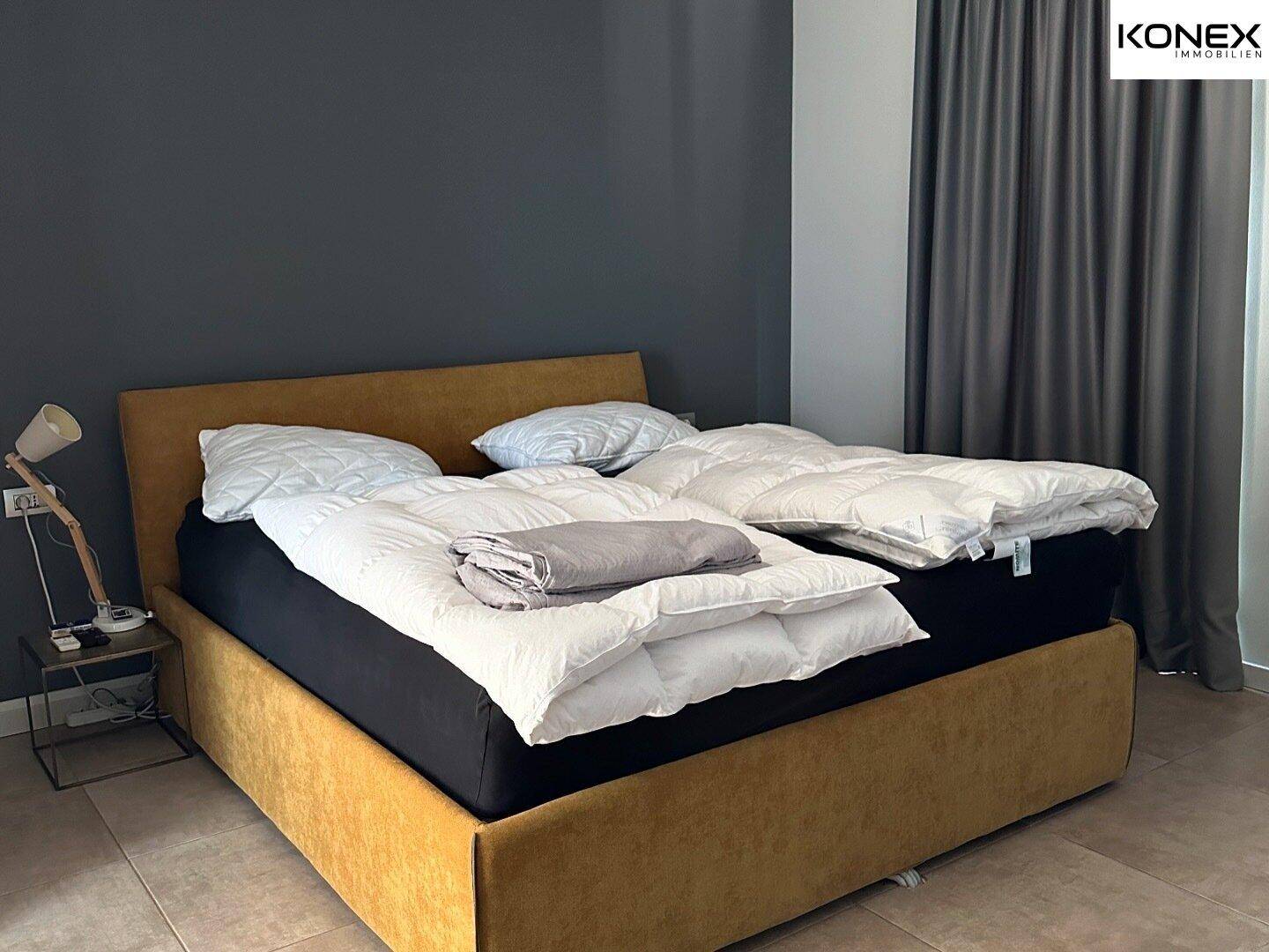 Schlafzimmer mit großem Bett, dunkler Akzentwand und Fliesenboden für erholsame Nächte.