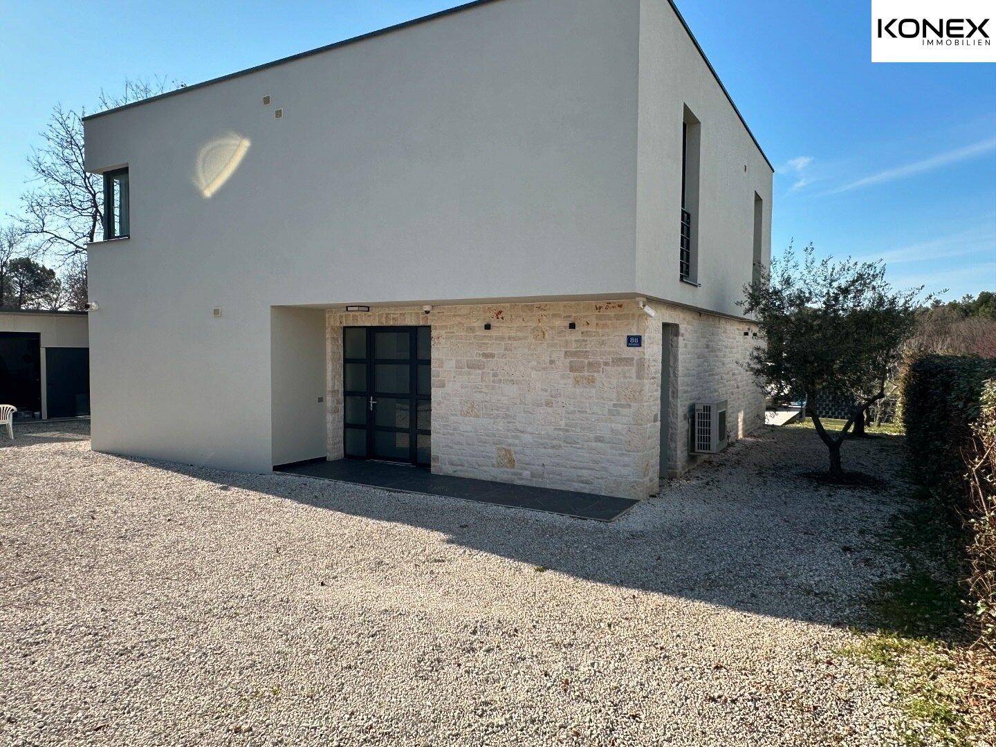 Moderne Hausfassade mit Kiesauffahrt und einladendem Eingangsbereich.