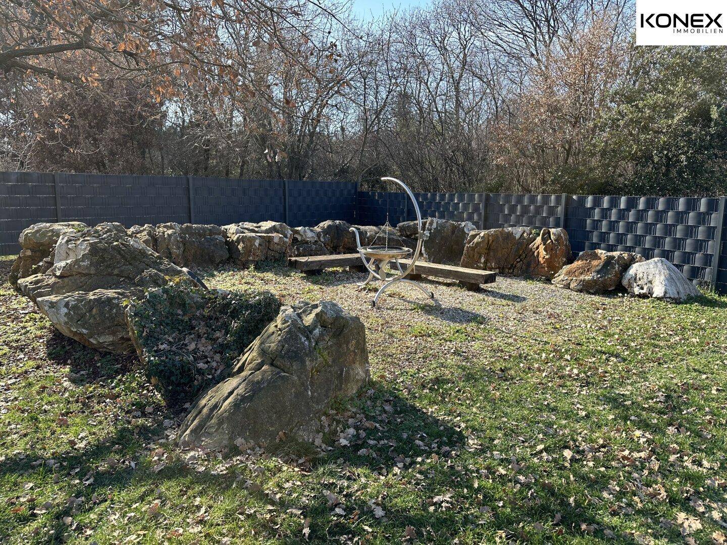 Naturnaher Gartenbereich mit großen Felsen und einer Feuerstelle für gemütliche Abende.
