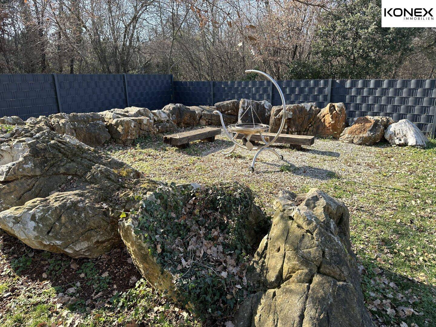 Gepflegter Garten mit Steinformationen und einer zentralen Feuerstelle im Freien.