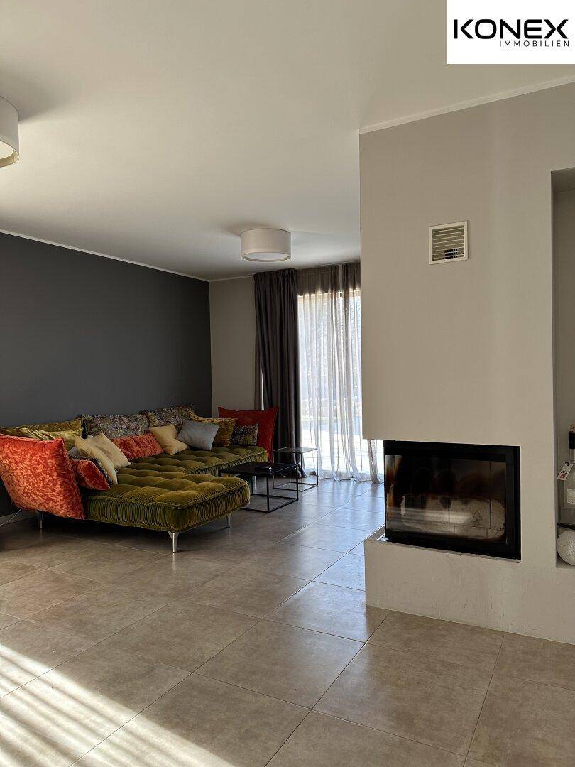 Helles Wohnzimmer mit modernem Kamin, bequemer Couch und Zugang zum Außenbereich.