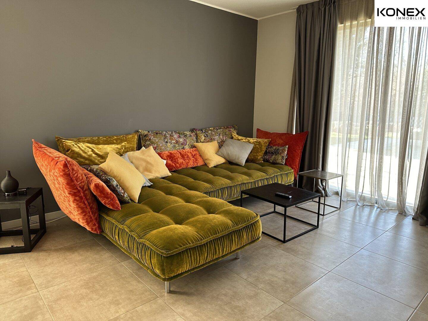Gemütliches Wohnzimmer mit großem, farbenfrohem Sofa, Fliesenboden und viel Tageslicht.