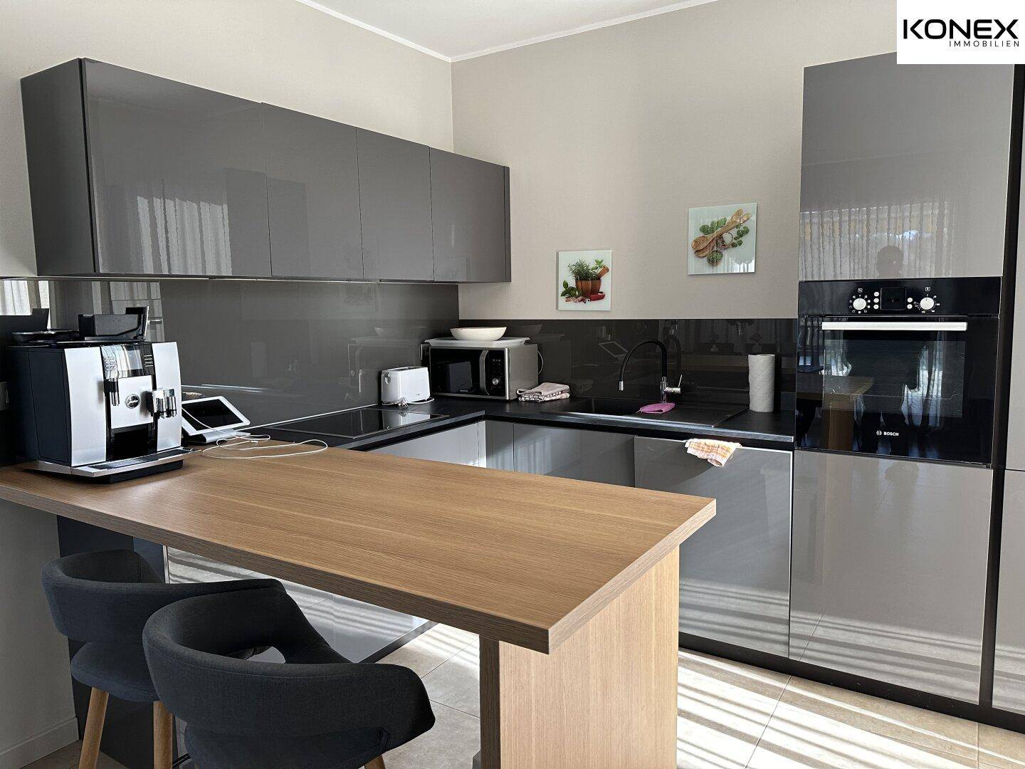 Moderne Küche mit grauen Hochglanzfronten, integrierten Geräten und praktischer Frühstücksbar.