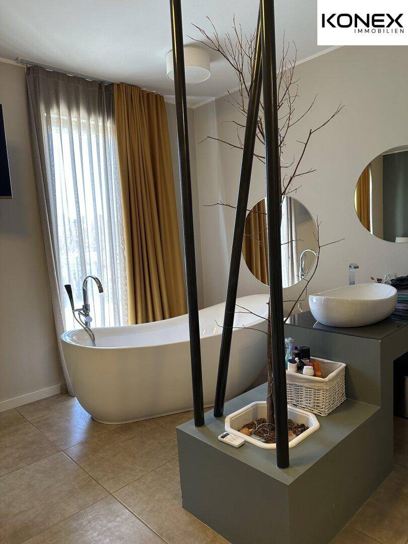 Geräumiges Badezimmer mit freistehender Badewanne, modernem Waschbecken und Fliesenboden.