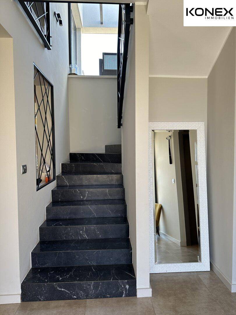 Elegante Treppe mit dunklen Marmorstufen und modernem Metallgeländer im Eingangsbereich.
