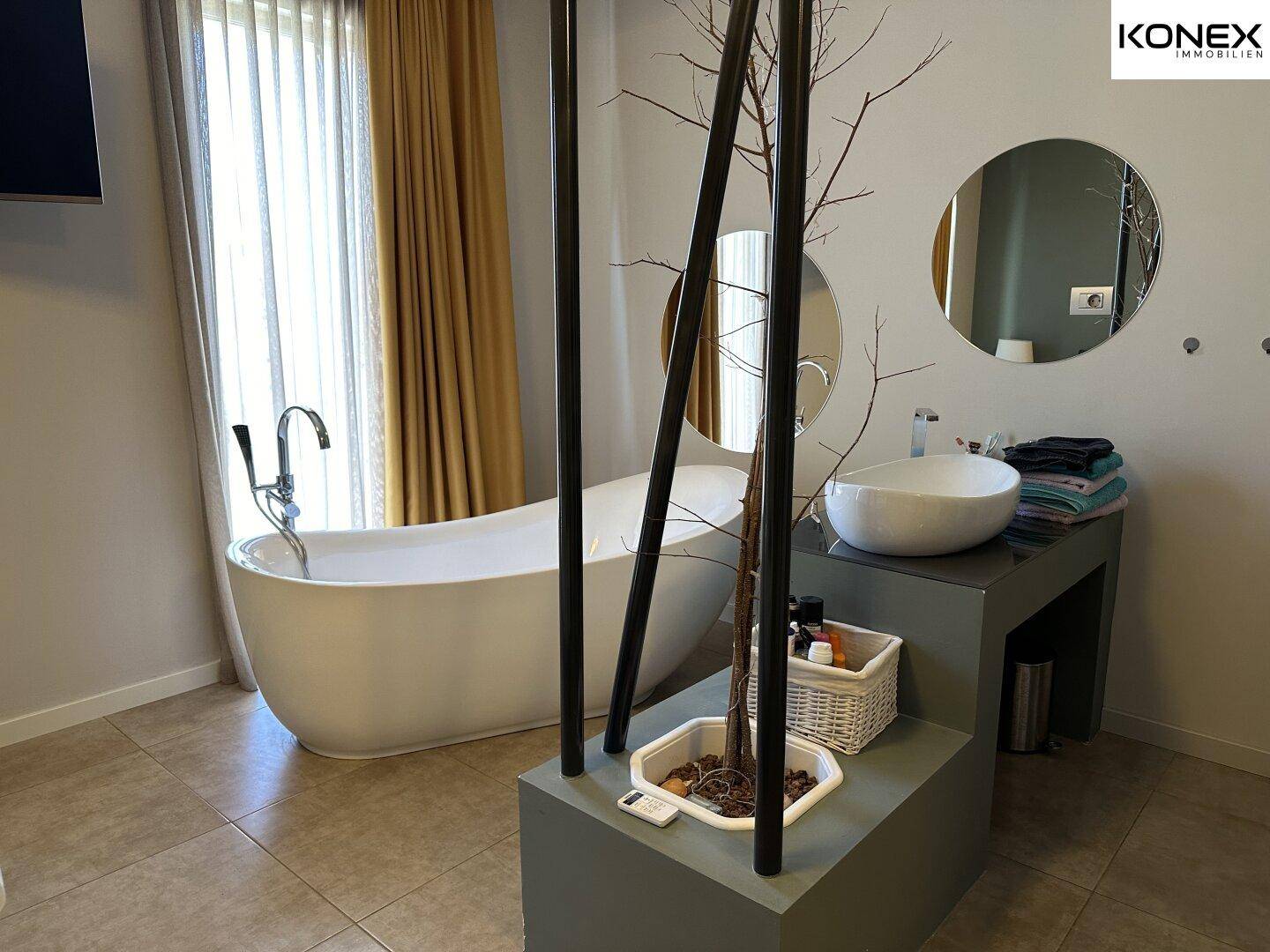 Geräumiges Badezimmer mit freistehender Badewanne, modernem Waschbecken und Fliesenboden.