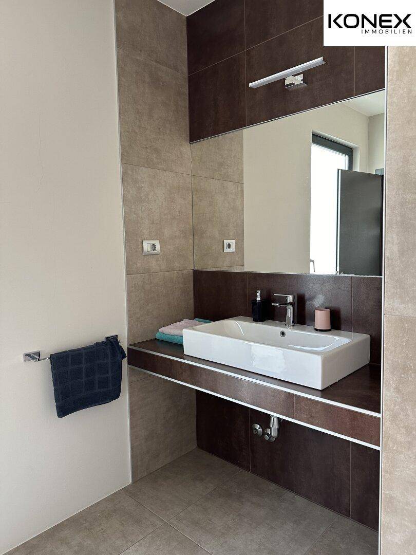Modernes Badezimmer mit elegantem Waschbecken, großem Spiegel und stilvollen Fliesen.