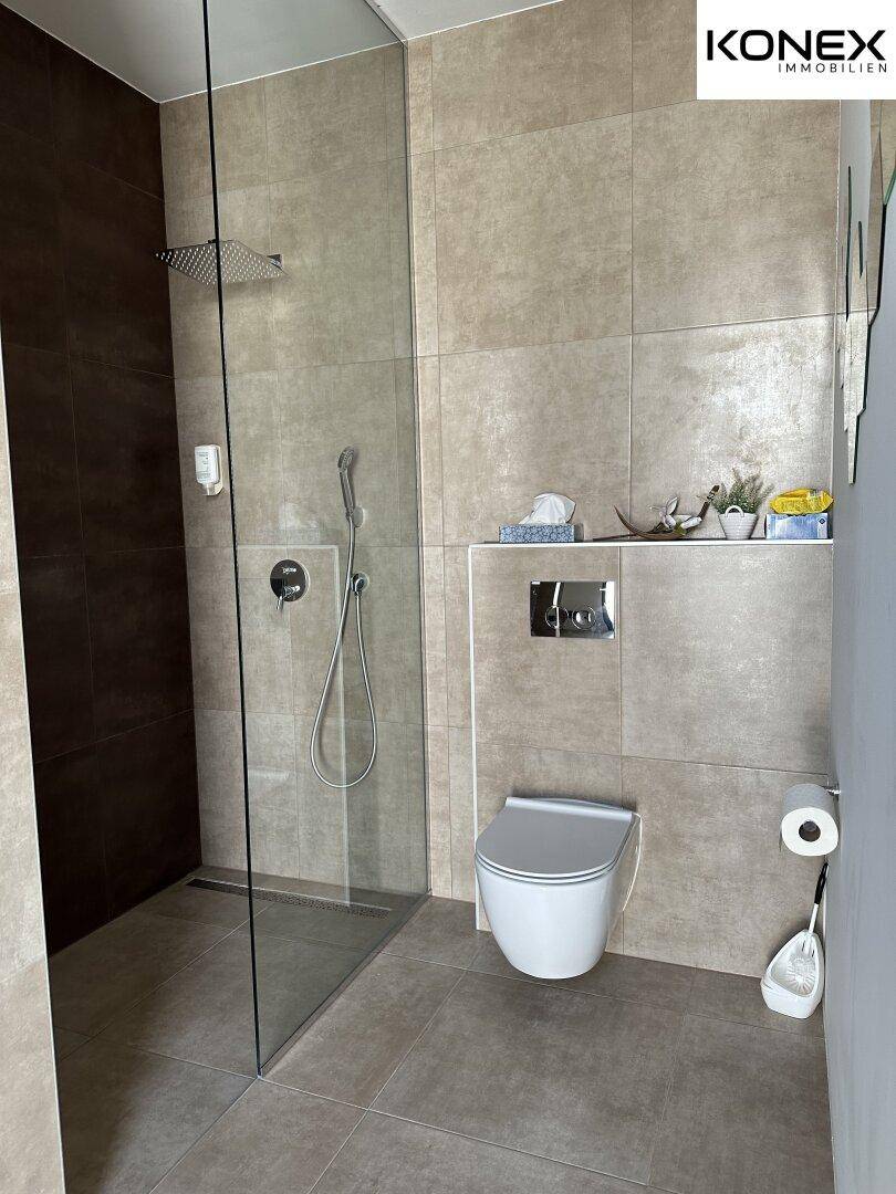 Modernes Badezimmer mit ebenerdiger Dusche, Wand-WC und großformatigen Fliesen.