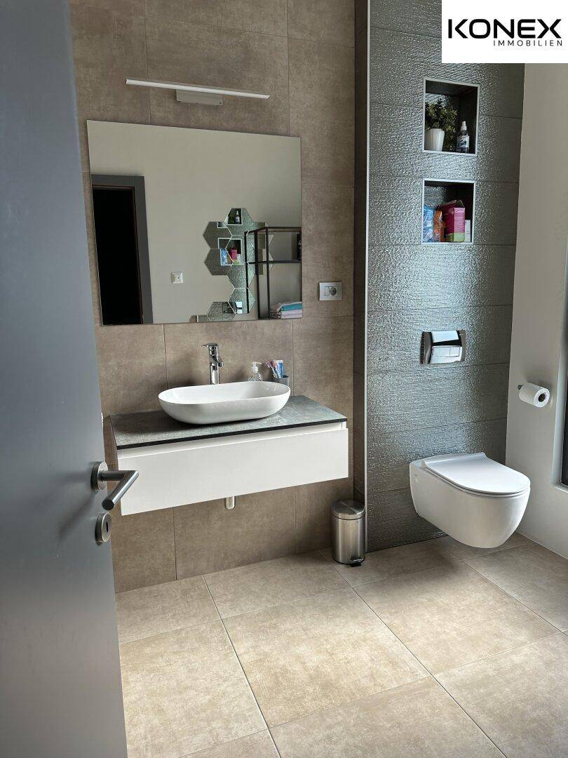Helles Badezimmer mit modernem Waschbecken, Wand-WC und großem Spiegel.