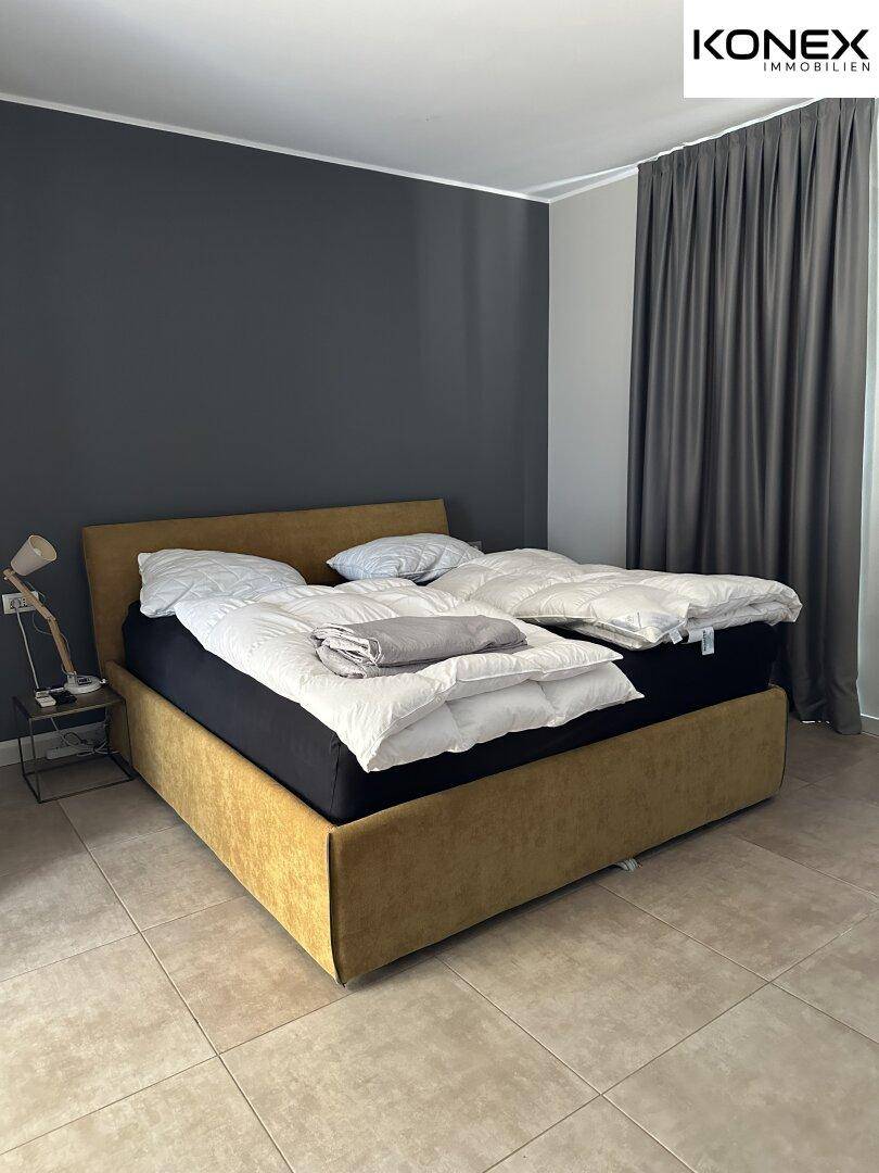 Schlafzimmer mit großem Bett, dunkler Akzentwand und Fliesenboden für erholsame Nächte.