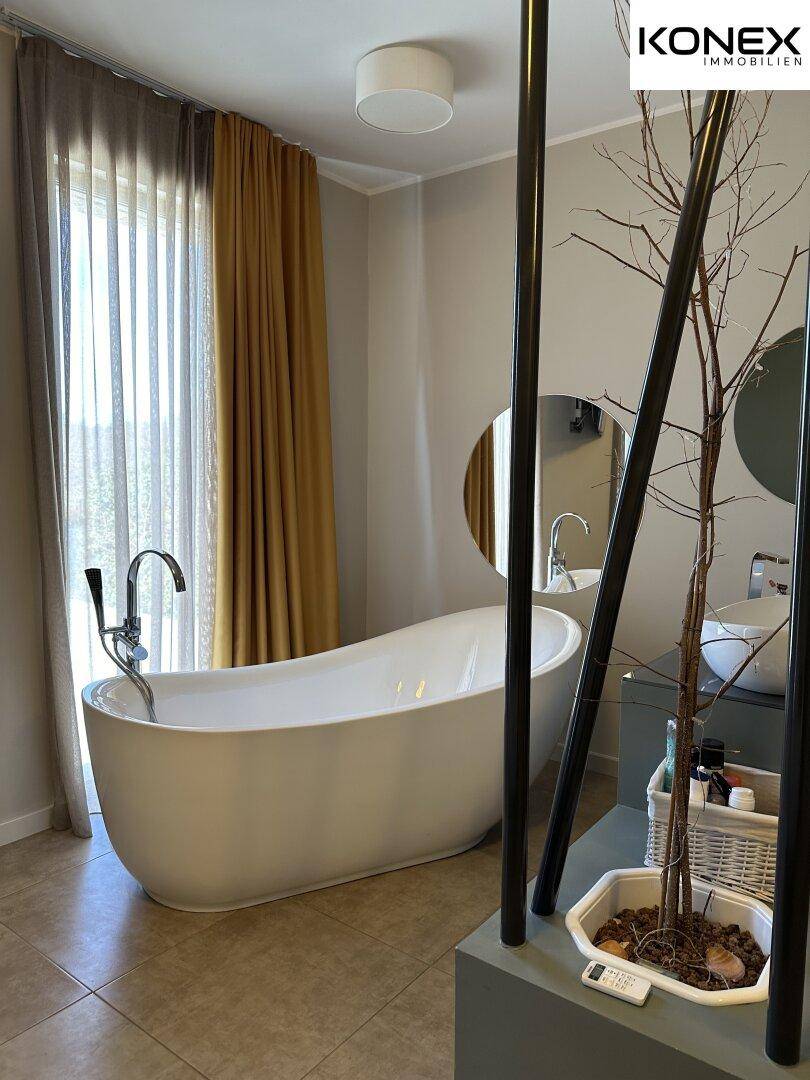 Geräumiges Badezimmer mit freistehender Badewanne, modernem Waschbecken und Fliesenboden.