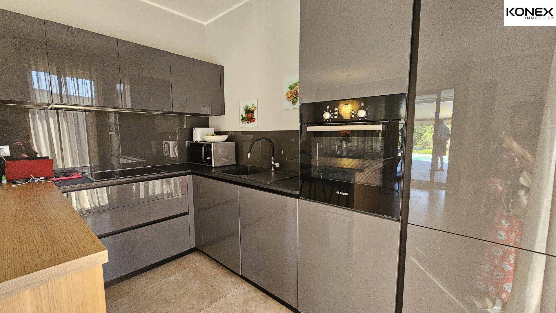 Moderne Küche mit grauen Hochglanzfronten, integriertem Backofen und viel Arbeitsfläche.