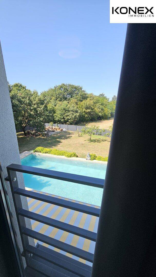 Blick aus dem Fenster auf den Swimmingpool und die grüne Umgebung.