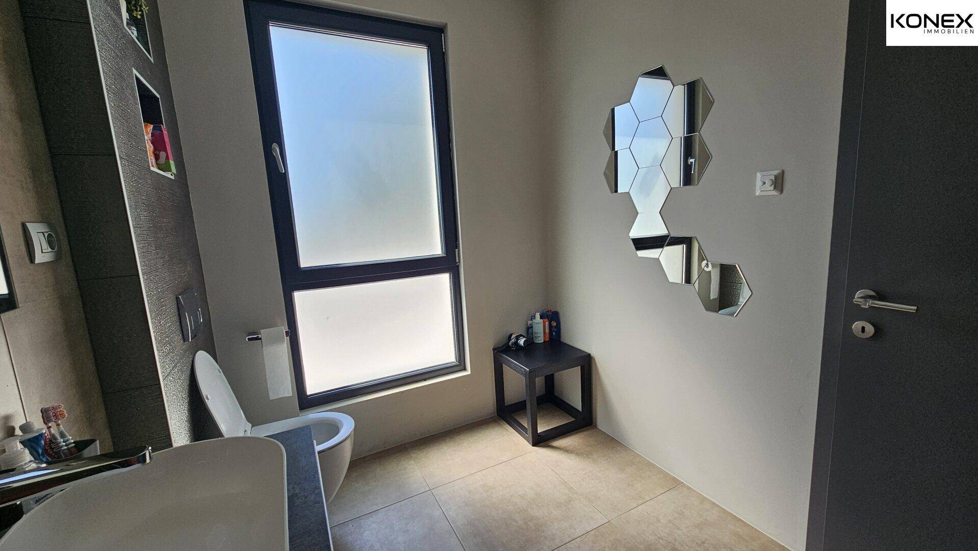 Modernes Badezimmer mit WC, Fenster und dekorativen Spiegeln.