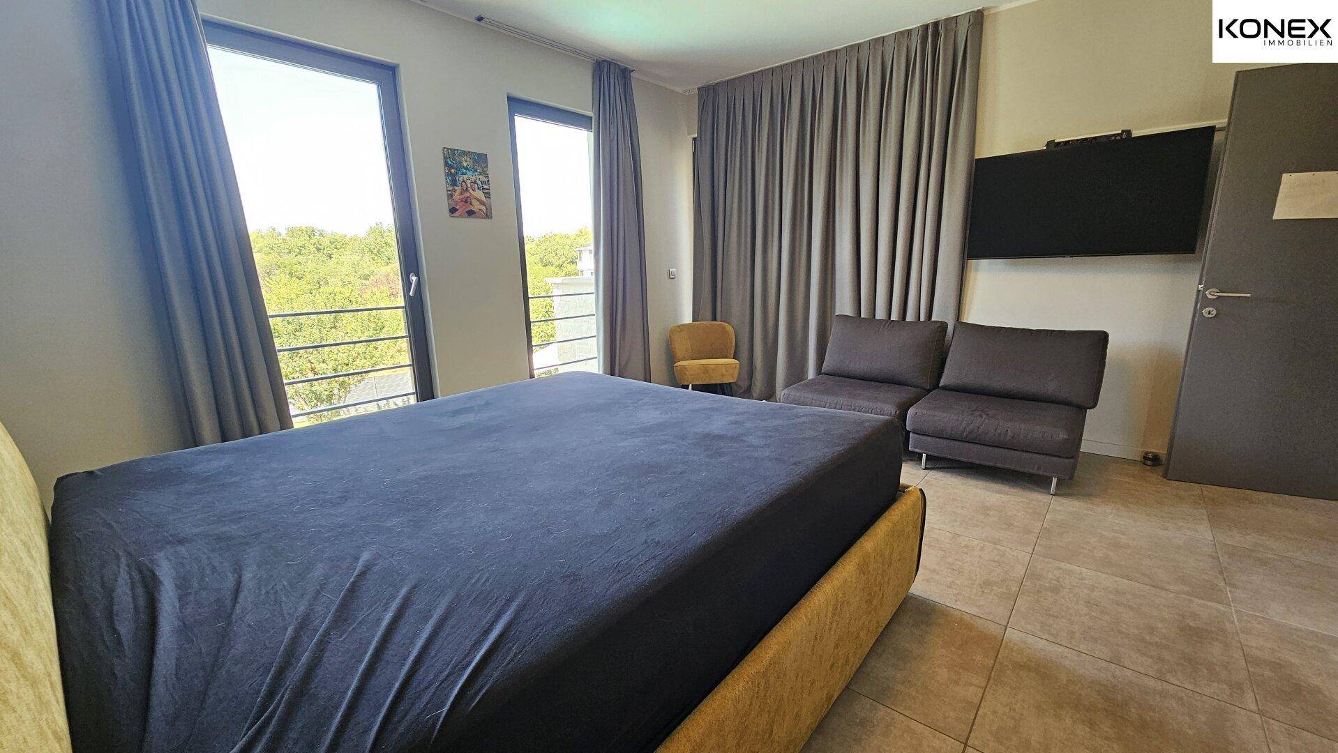 Geräumiges Schlafzimmer mit großem Bett, Sitzgelegenheiten und großen Fenstern.