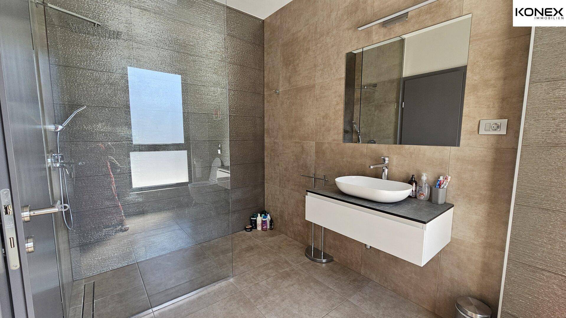 Modernes Badezimmer mit ebenerdiger Dusche, elegantem Waschbecken und großem Spiegel.