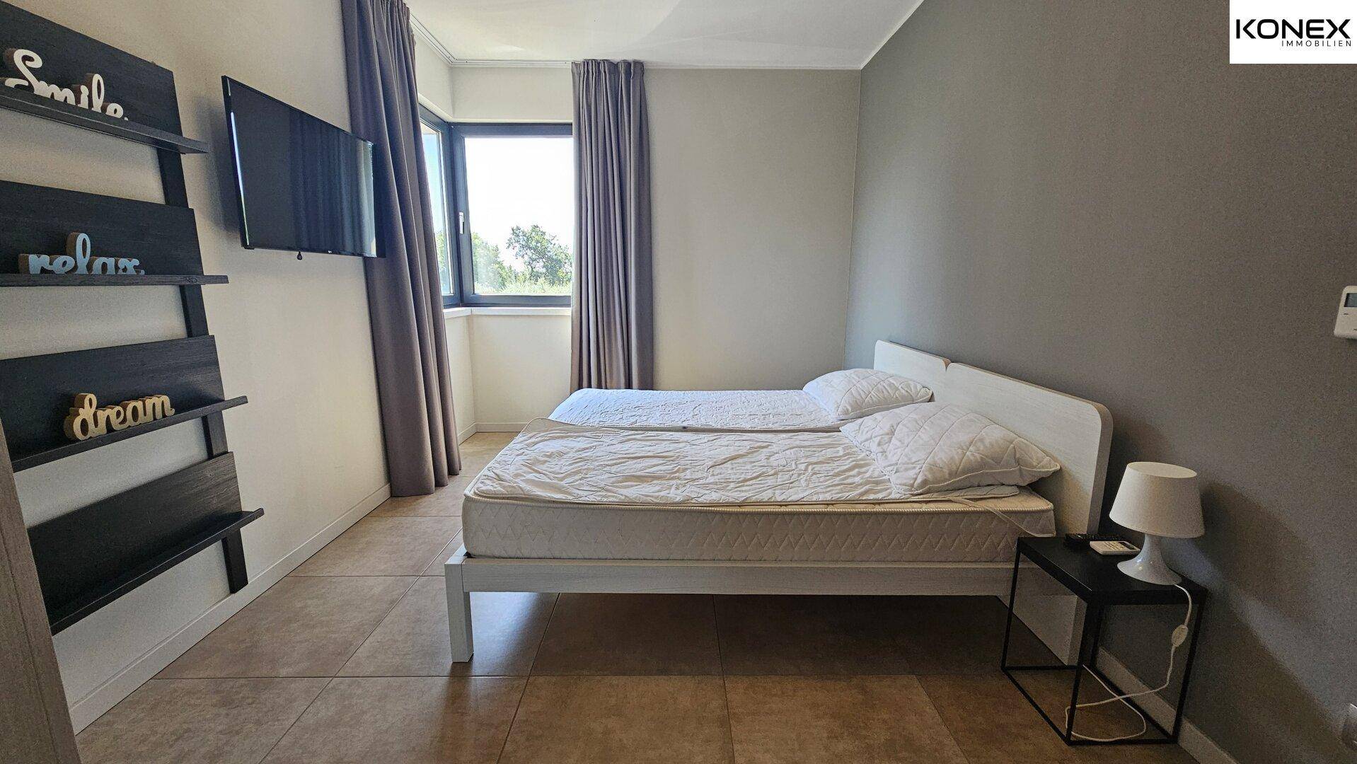 Schlafzimmer mit zwei Einzelbetten, Fenster und Wandfernseher.