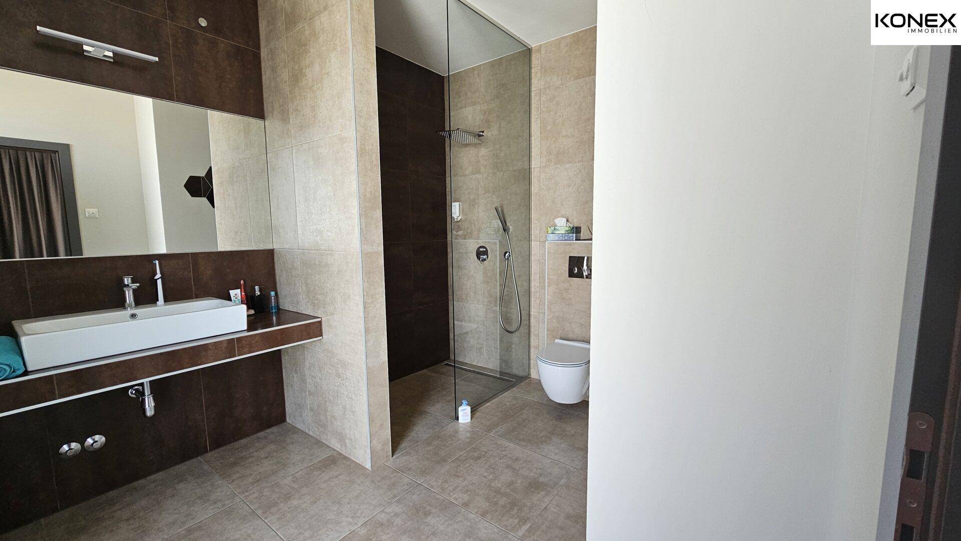 Modernes Badezimmer mit ebenerdiger Dusche, elegantem Waschbecken und großem Spiegel.