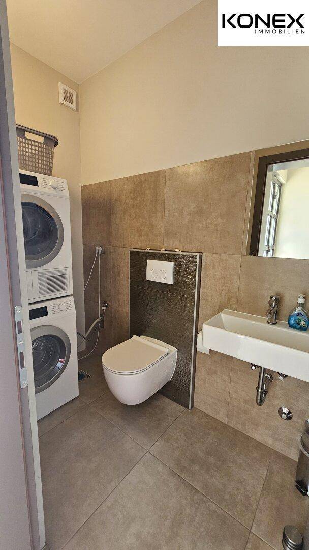 Modernes Badezimmer mit Waschmaschine, Trockner, WC und Waschbecken.