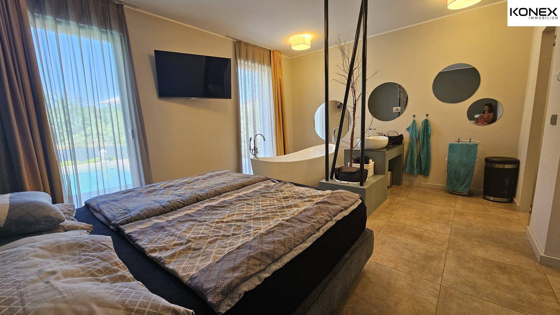 Geräumiges Schlafzimmer mit Badewanne, Waschbecken und Blick auf den Pool.
