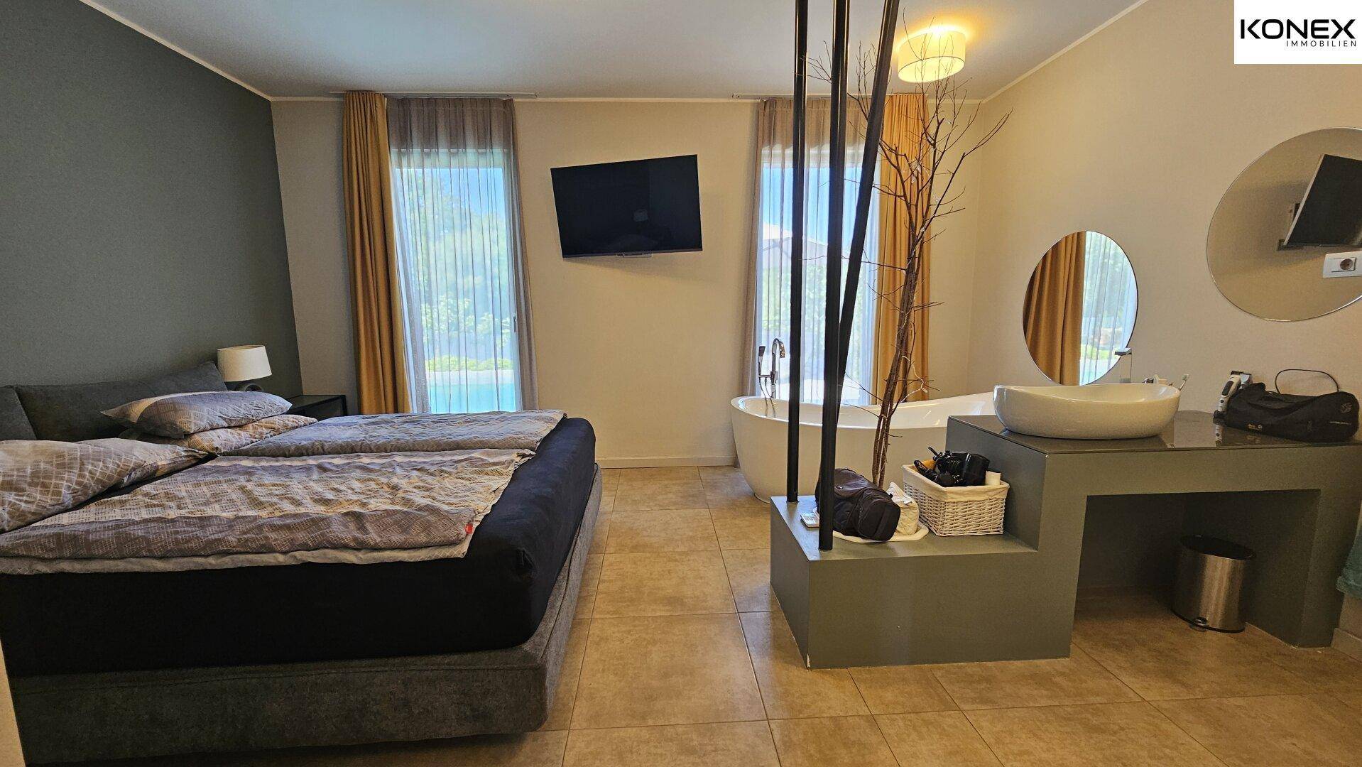 Geräumiges Schlafzimmer mit Badewanne, Waschbecken und Blick auf den Pool.