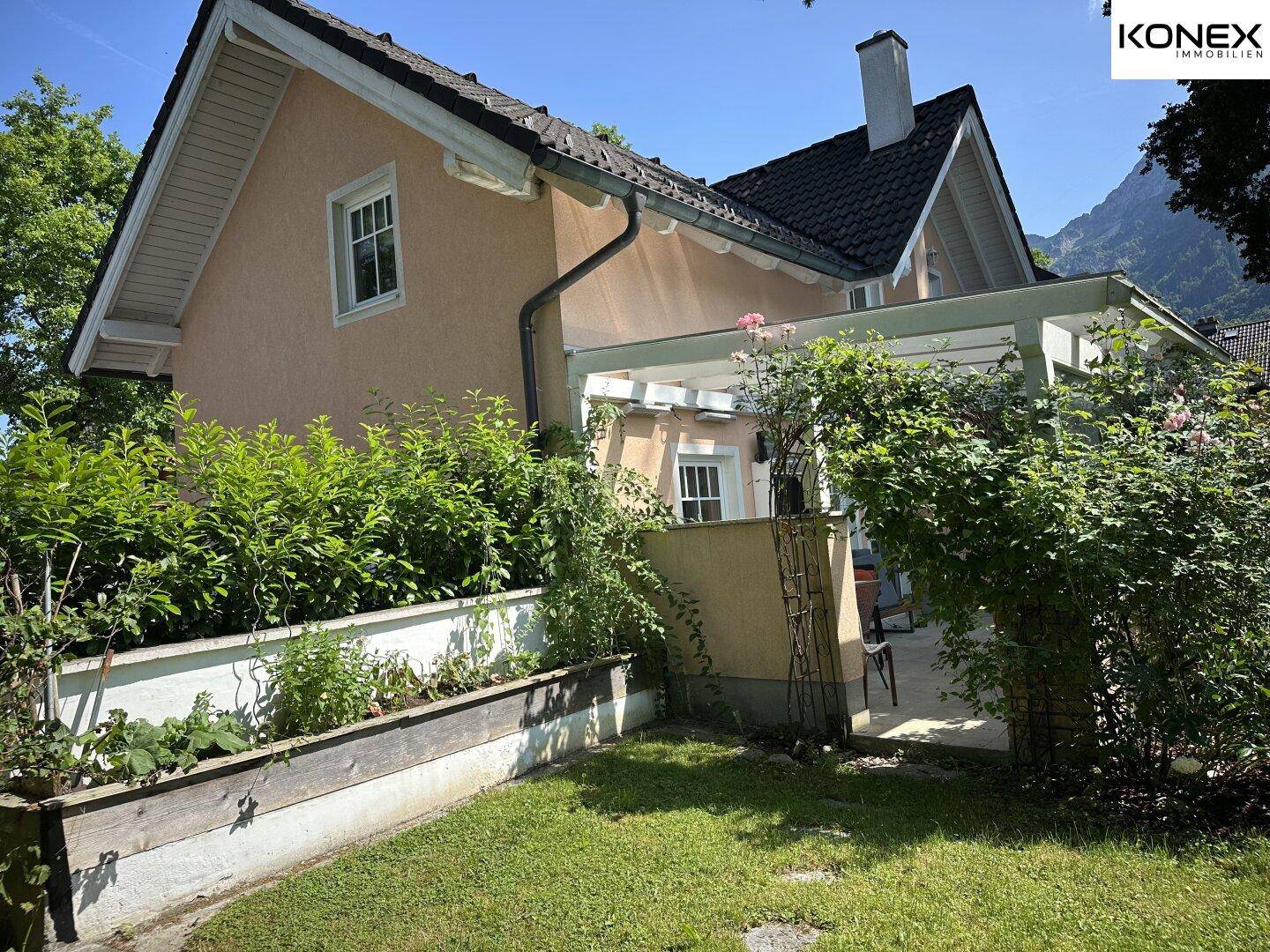 Seitenansicht des Hauses mit einem Hochbeet und dichtem Grün, das den Garten umgibt.