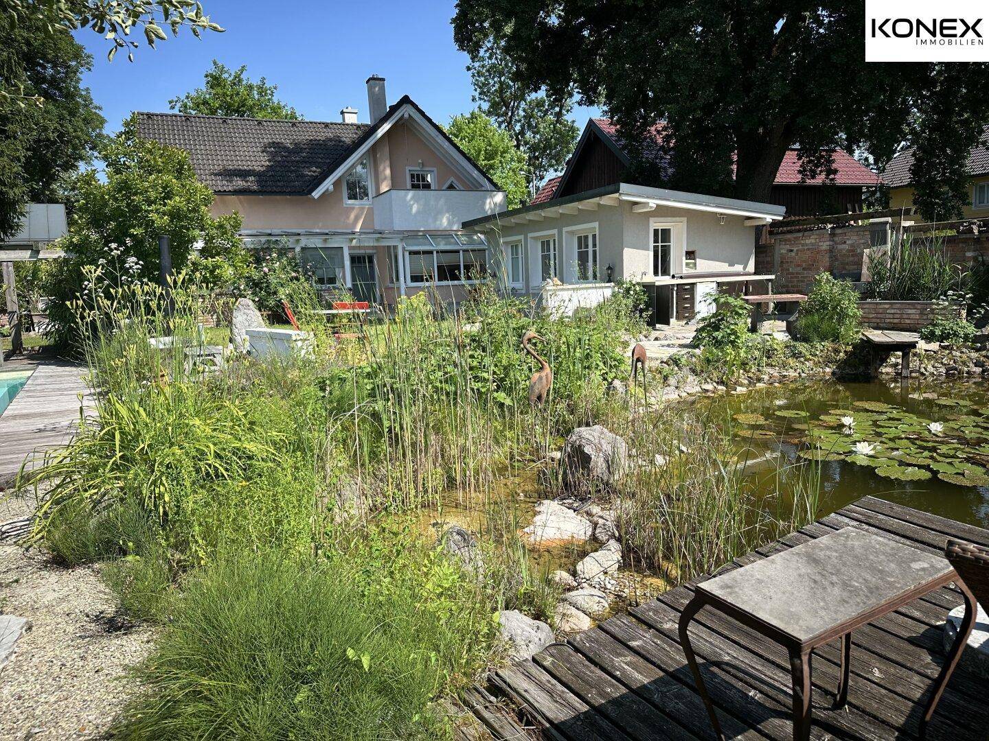 Weitläufiger Garten mit Haupthaus, Nebengebäude und einem naturnahen Teich.