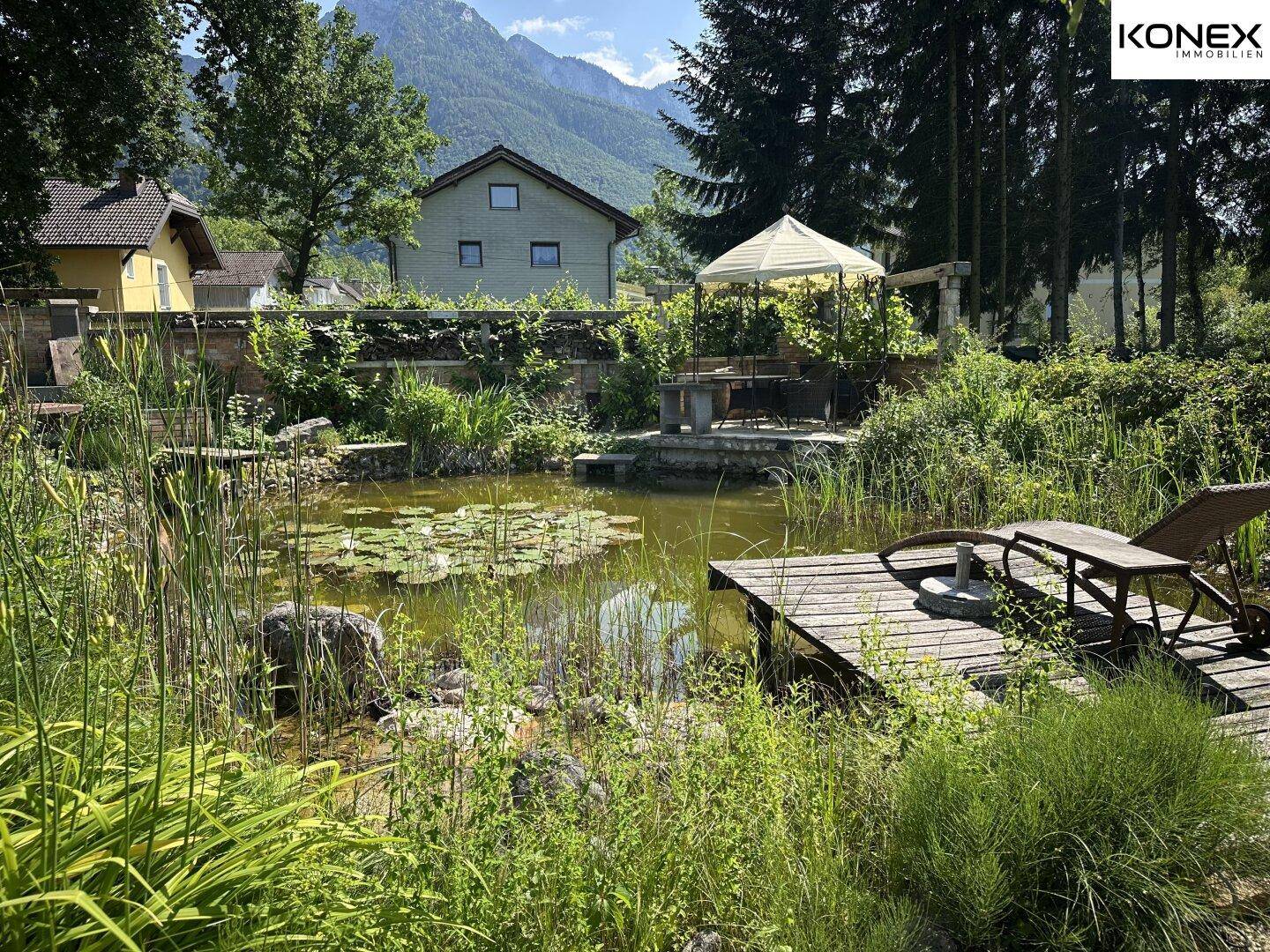 Idyllischer Gartenteich mit Liegestuhl auf Holzsteg und malerischem Bergblick.