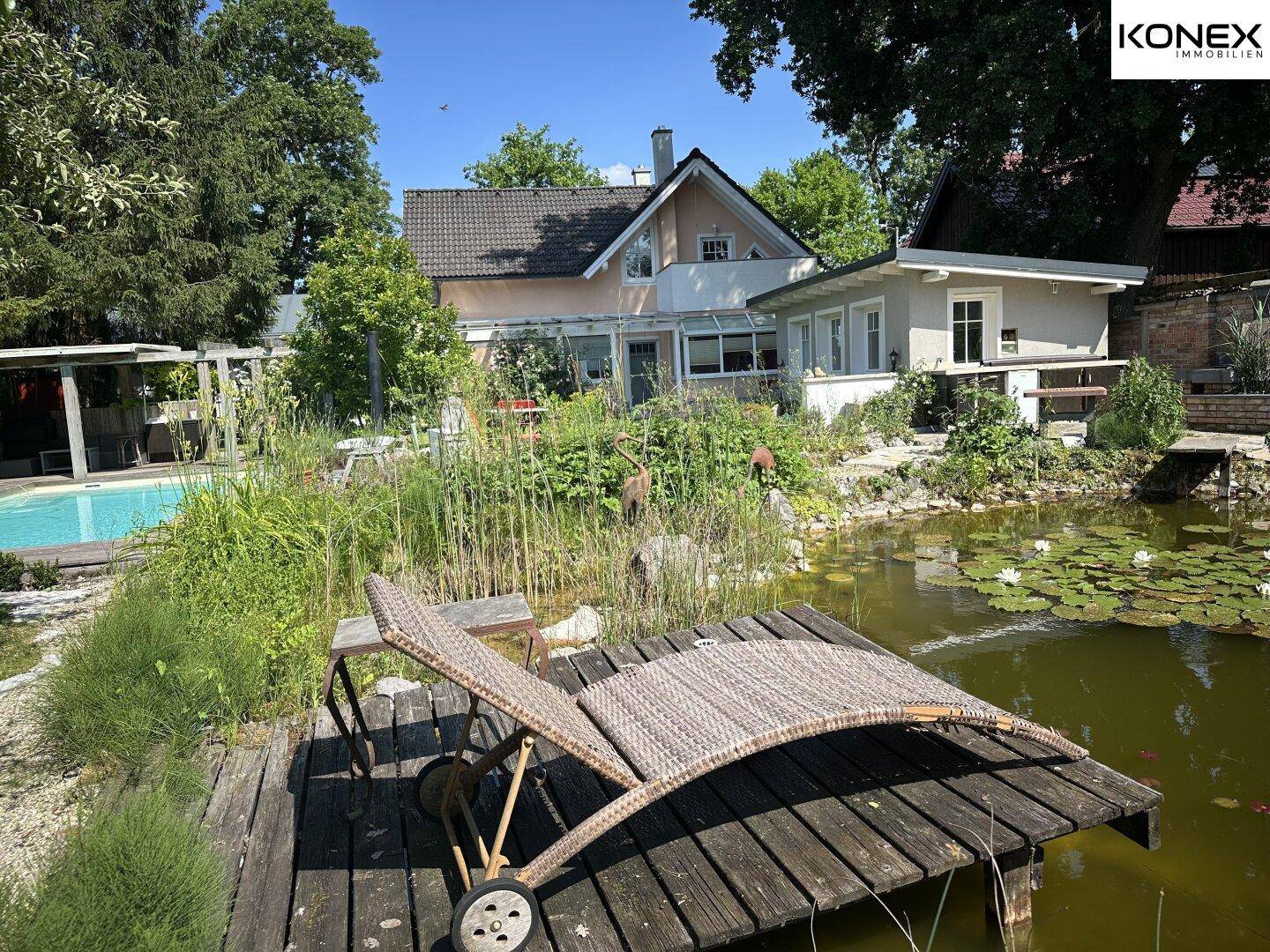 Weitläufiger Garten mit Teich, Liegestuhl auf Holzsteg und Blick auf das Wohnhaus.