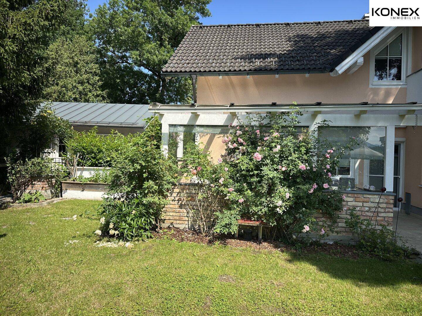 Seitenansicht des Hauses mit einem grünen Rasen und blühenden Rosensträuchern.