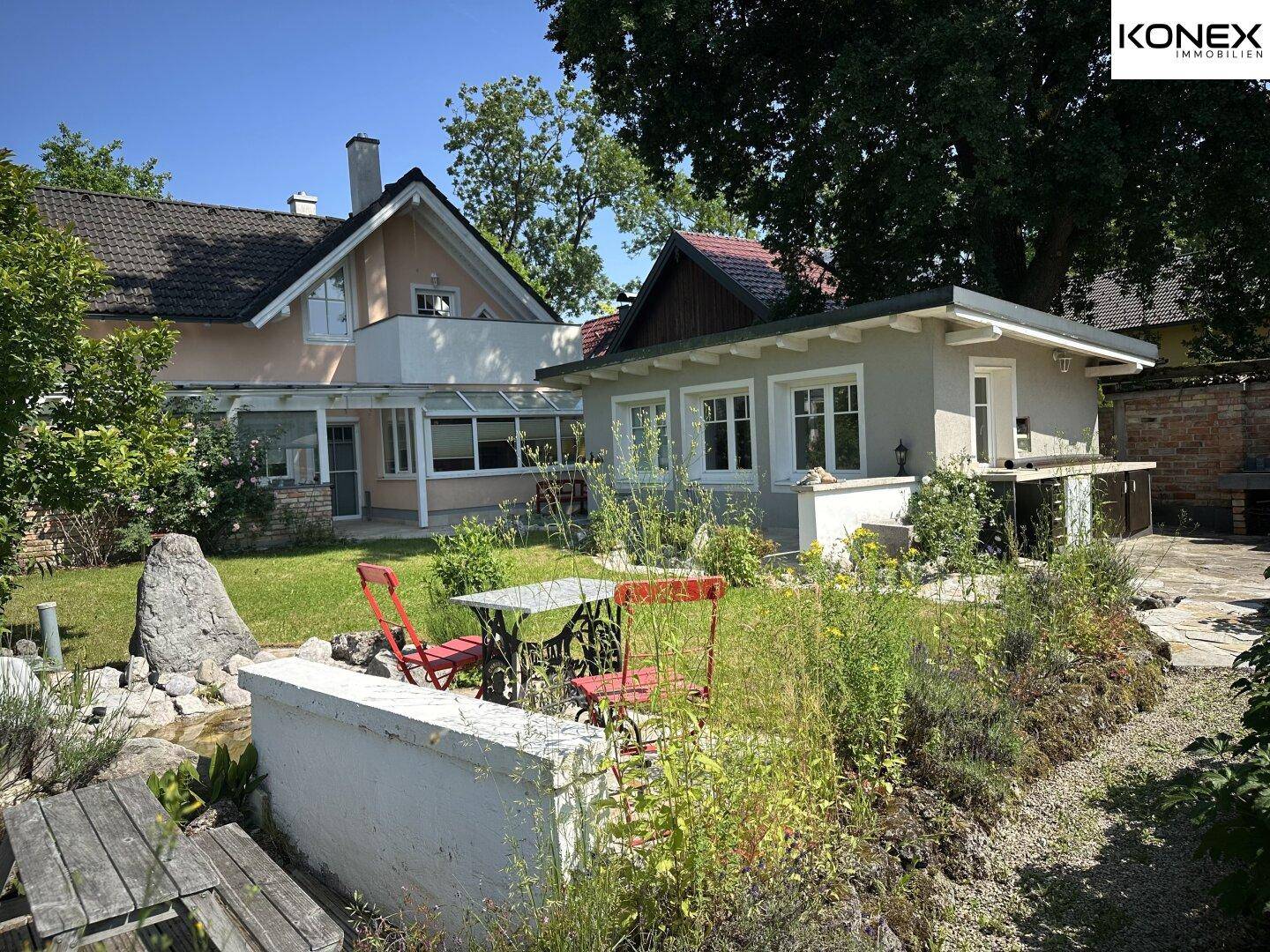Weitläufiger Garten mit Haupthaus und Nebengebäude, umgeben von vielfältiger Bepflanzung.