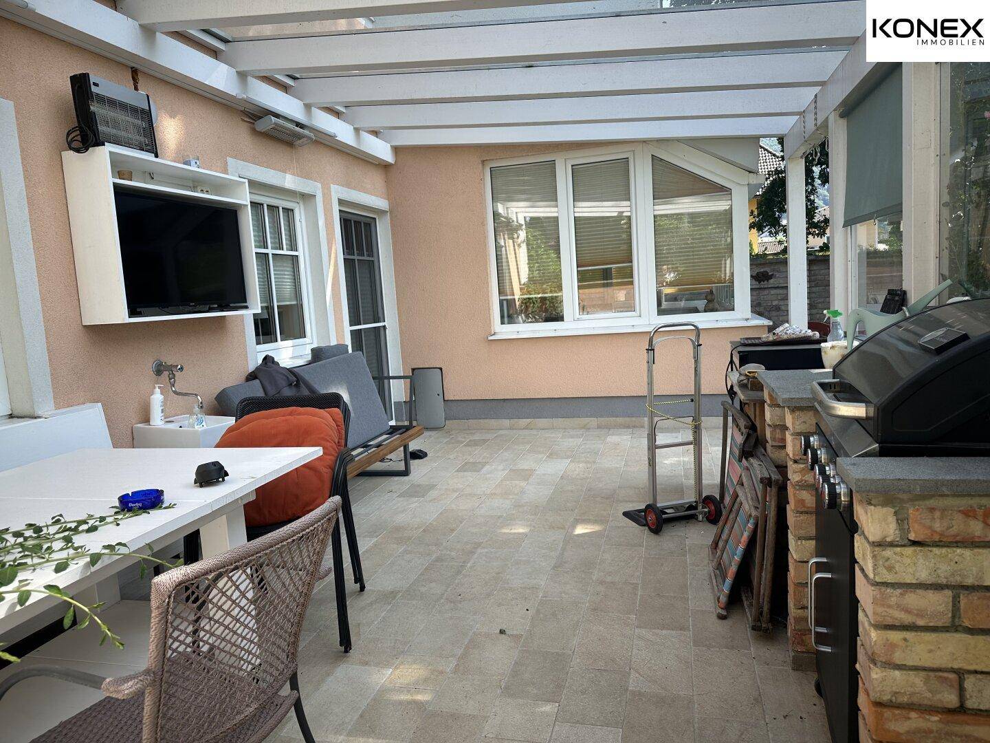 Überdachte Terrasse mit Essbereich, Grill und Blick in den Garten.