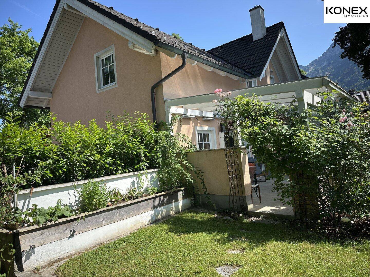 Seitenansicht des Hauses mit einem Hochbeet und dichtem Grün, das den Garten umgibt.