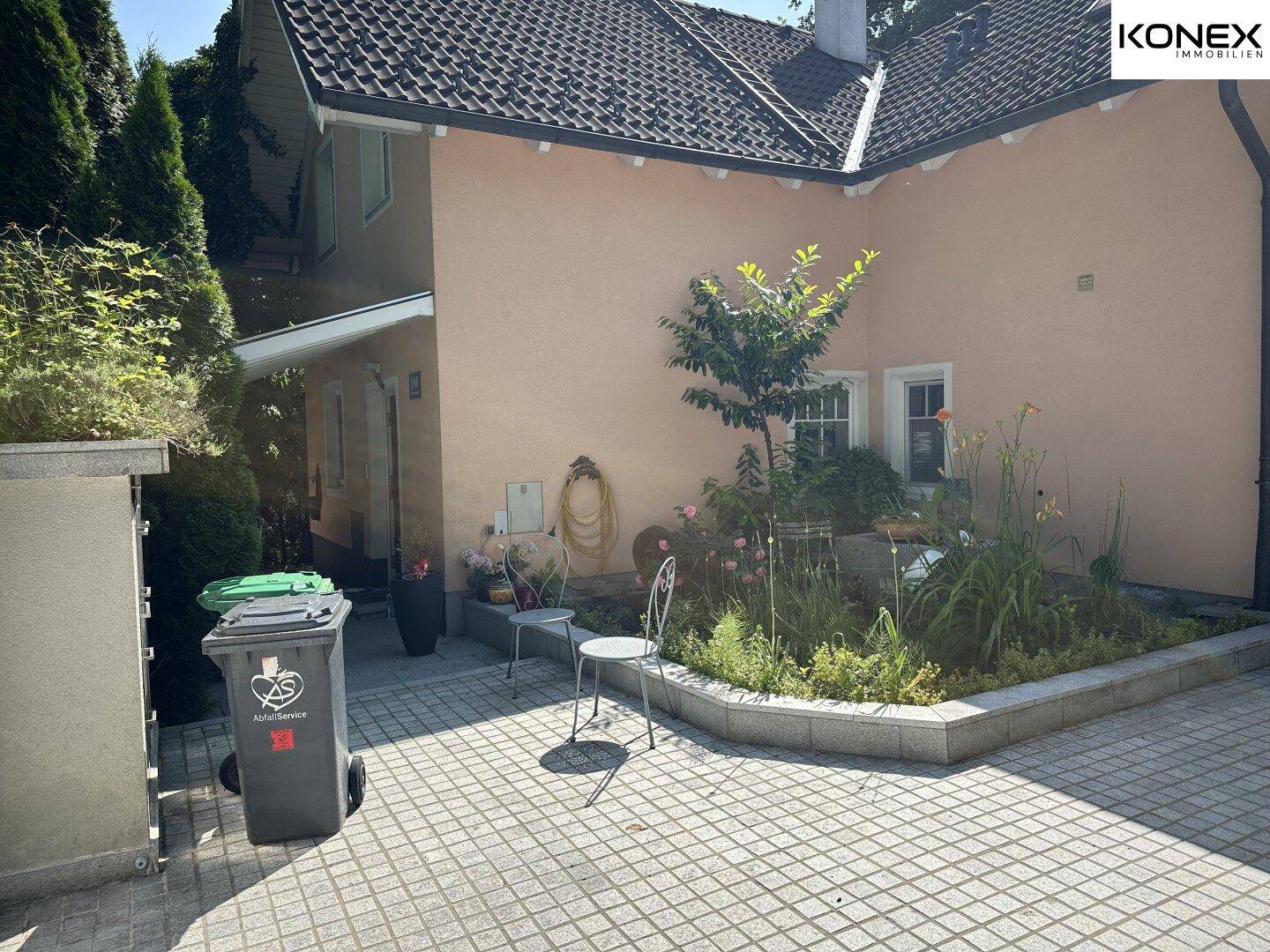 Geräumige Einfahrt mit gepflastertem Boden und einem kleinen Blumenbeet am Haus.