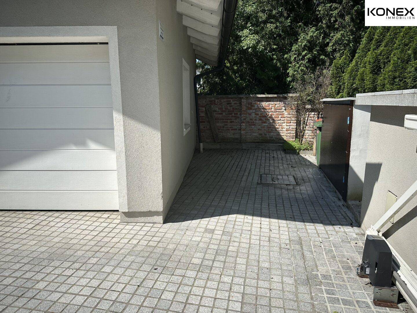 Schmaler gepflasterter Weg neben der Garage, der zum hinteren Bereich führt.