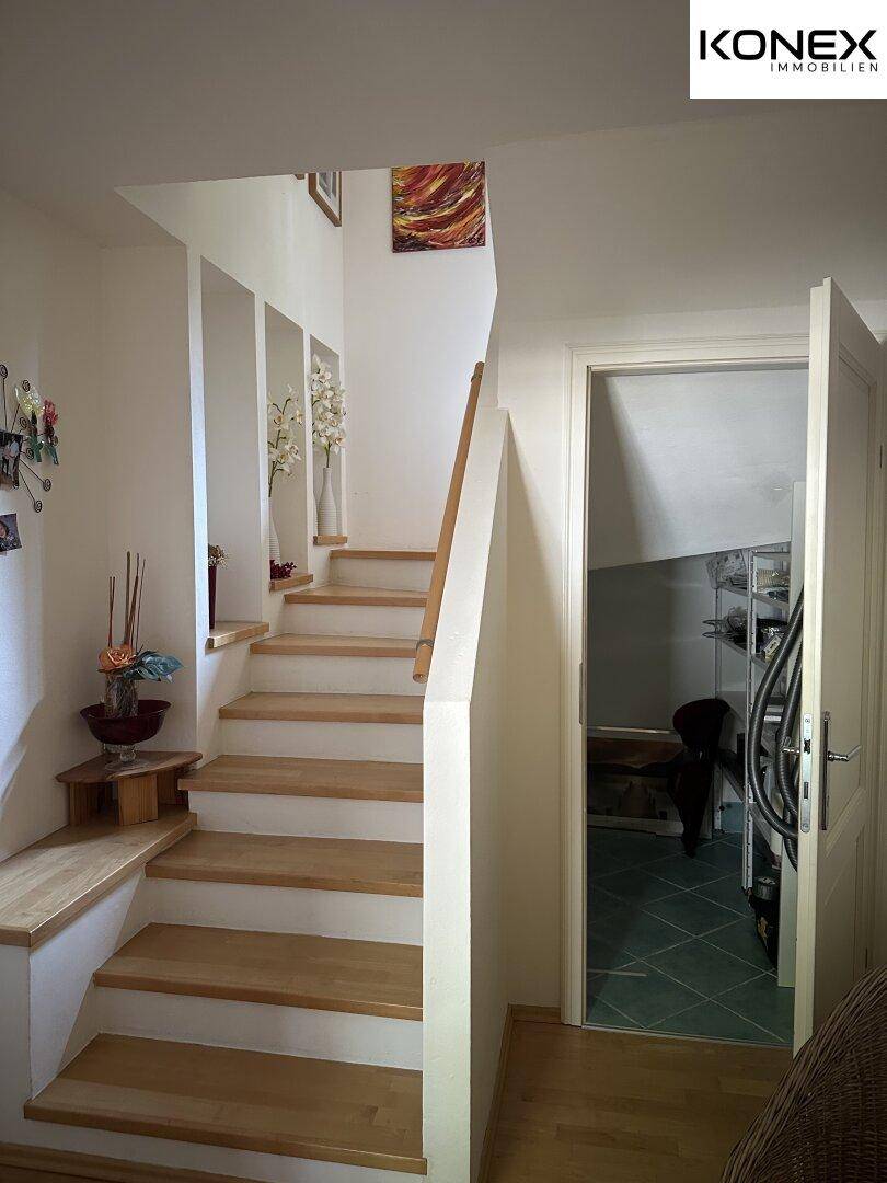 Heller Treppenaufgang mit Holzstufen und weiß gestrichenen Wänden.