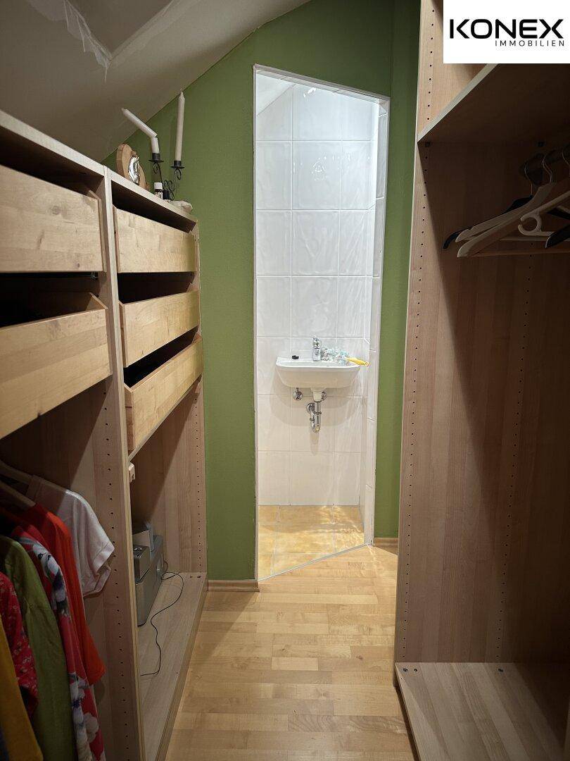 Begehbarer Kleiderschrank mit offenen Regalen und kleinem Waschbecken im Hintergrund.