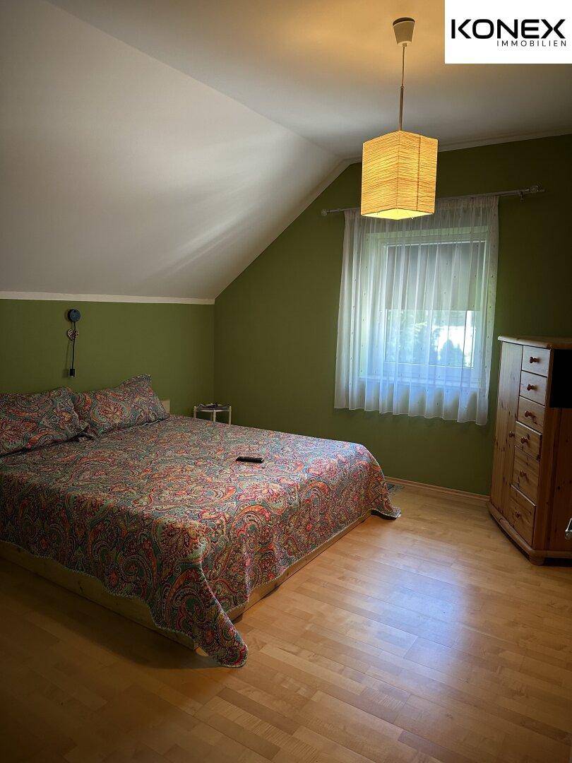 Schlafzimmer mit grün gestrichenen Wänden, Holzboden und Dachschräge.