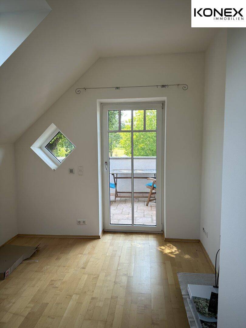 Leerer Raum mit Holzboden und Zugang zu einem kleinen Balkon.