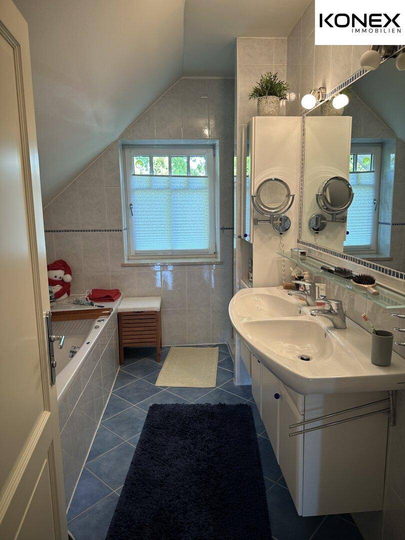 Helles Badezimmer mit Doppelwaschbecken, Badewanne und Fenster.