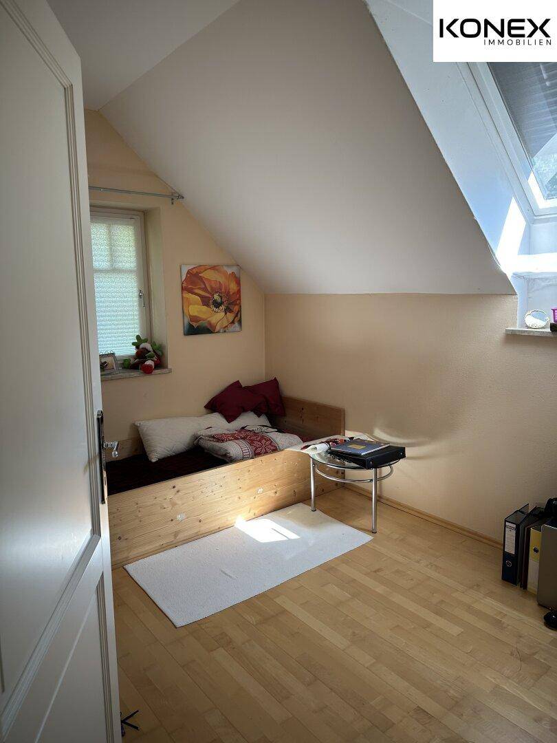 Kleines Schlafzimmer mit Holzbett, Dachschräge und Fenster.