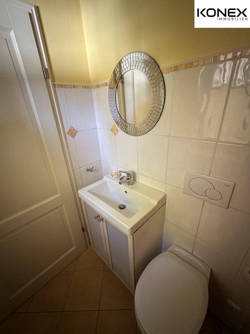 Kleines Gäste-WC mit Waschbecken, Toilette und Spiegel.