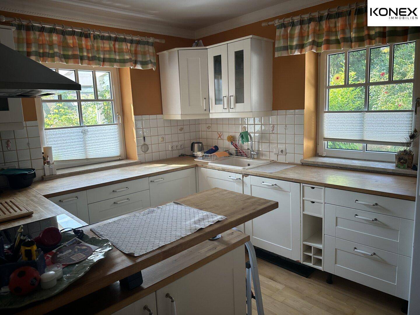 Helle Küche mit weißen Schränken, Holz-Arbeitsplatten und zwei Fenstern.