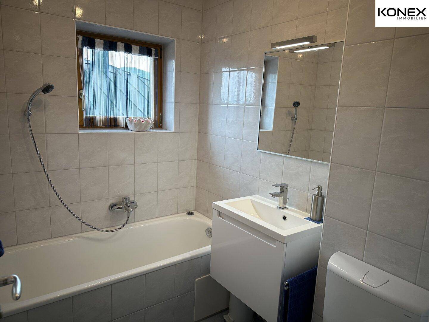 Gefliestes Badezimmer mit Badewanne, Waschbecken und Fenster für gute Belüftung.