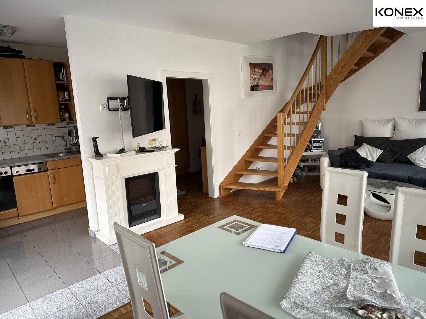 Offener Wohn- und Essbereich mit Kamin, Holztreppe und angrenzender Küche.