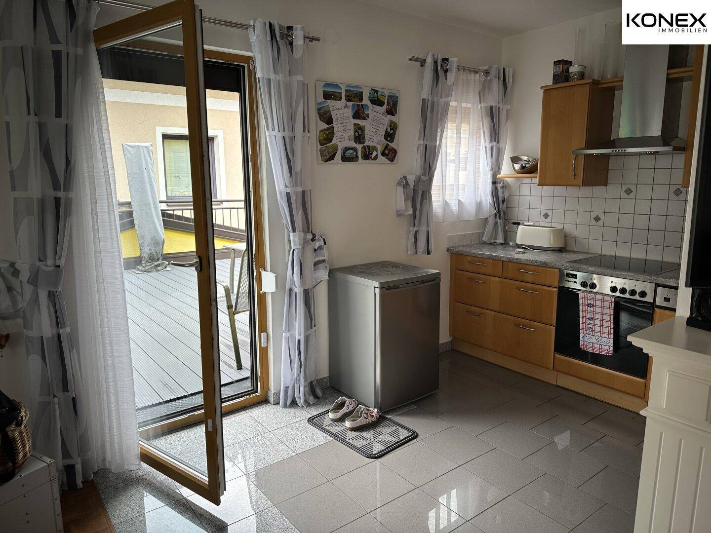 Kleine Küche mit Fliesenboden, Kühlschrank und direktem Zugang zur Außenterrasse.